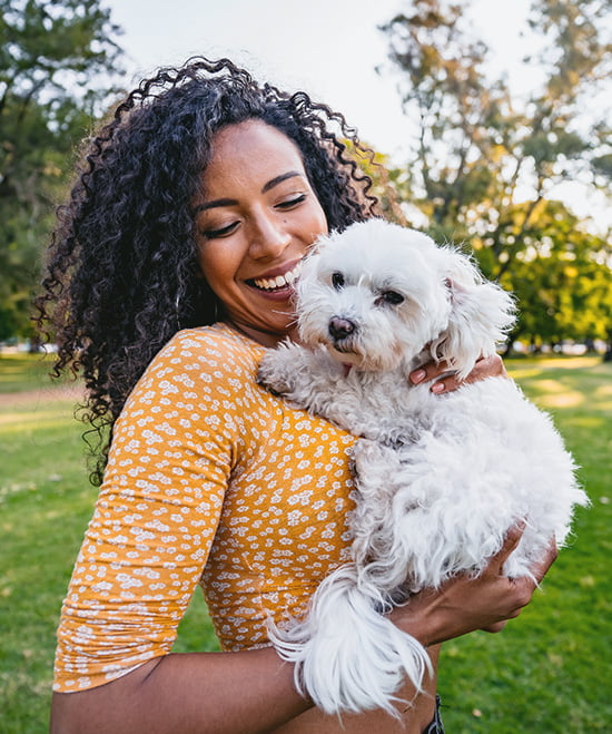 Woman smiling, looking down at a small white dog that she is holding.